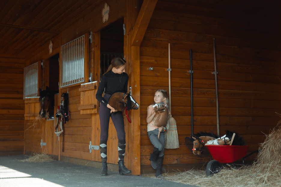 Jongeren met Hobby Horses buiten de houten stallen van een rijvereniging