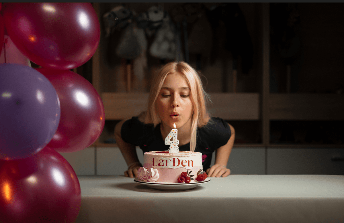 Lara blaast een kaarsje met het cijfer vier uit op een LarDen-verjaardagstaart naast kleurrijke ballonnen