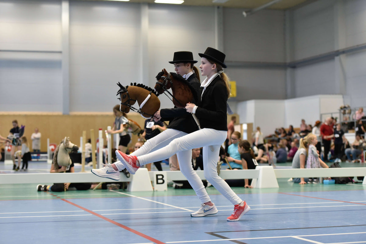 Twee kinderen in formele Hobby Horsing-kleding doen binnen mee met Hobby Horses