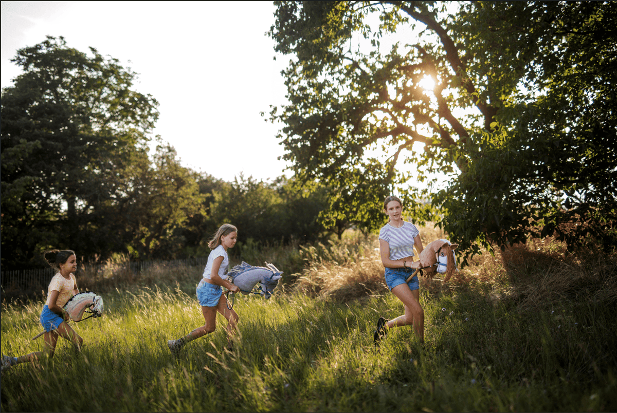 Kinderen rennen met Hobby Horses door een zonnig grasveld