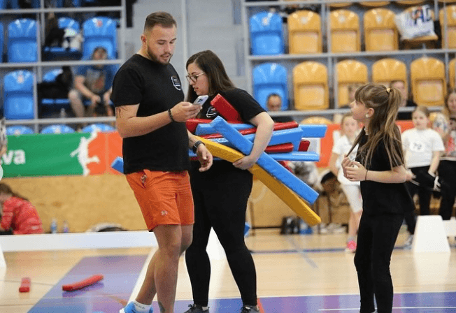 Denny maakt samen met een jonge deelnemer kleurrijke Hobby Horse-hindernissen klaar in een sporthal