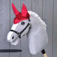 Grijze Hobby Horse van Hobby Horse LarDen met witte manen, zwart hoofdstel en Oornetje gehaakt rood voor bescherming tegen vliegen, staand tegen een licht houten achtergrond.