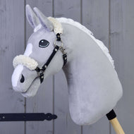 Zwart halster met bont - kunstleer van Hobby Horse LarDen, een grijs pluchen paard met witte manen en zwart halster op een houten stok, tegen een achtergrond van houten panelen.