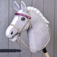 Hobby Horse van Hobby Horse LarDen met grijze vacht, witte manen, zwart oog en de Bordeaux kunstleer set - hoofdstel, teugels en martingaal, plus een paarse frontriem en een gezicht in cartoonstijl. Het staat rechtop tegen een houten achtergrond.
