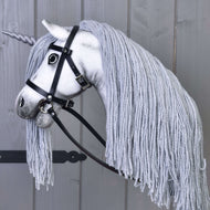 Hobby Horse Eenhoorn Silver met Hoofdstel en Halster van Hobby Horse LarDen met een wit gezicht, grijze manen van garen, lichtgrijze hoorn en zwart hoofdstel, gemonteerd op een stok en gefotografeerd tegen een houten achtergrond.