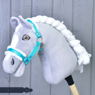 Een grijs-witte Hobby Horse met gevlochten witte manen draagt het "Halster turquoise met bont" van Hobby Horse LarDen, het perfecte accessoire, tegen een lichtgrijze houten achtergrond.