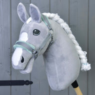 Halster grijs met mint bont van Hobby Horse LarDen — een grijs pluchen accessoire voor Hobby Horse met witte manen en aftekeningen op het gezicht — tegen een grijze houten achtergrond.