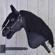 Hobby Horse Freya met Zwart Halster van Hobby Horse LarDen, met een witte gezichtsstreep en zwarte manen van garen op een houten stok, staat tegen een lichtgrijze houten wand, perfect voor elke paardenliefhebber in het gezin.