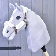 Bruin halster met compleet bont - kunstleer van Hobby Horse LarDen op een pluche, lichtgrijze Hobby Horse met witte manen en aftekeningen, op een houten stok en gefotografeerd tegen een achtergrond van grijze houten panelen.