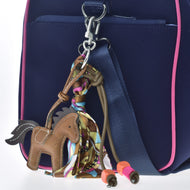 The Hobby Horse LarDen Keychain Horse Brown—adorned with a colorful scarf, orange and pink beads—accessorizes your navy blue bag with pink trim and blue strap, making it perfect for hobby horsing fans.