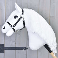 Hobby Horse Lady met zwart halster van Hobby Horse LarDen heeft een witte paardenkop met lange manen van garen, zwart halster en opvallende zwarte ogen op een houten stok, getoond tegen een grijze houten achtergrond.
