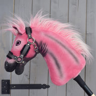 Een limited edition Hobby Horse LarDen Pinkie met een glinsterend halster van Hobby Horse LarDen is bevestigd op een stok en staat tegen een grijze houten muur.