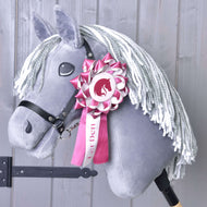 Hobby Horse Ribbon LarDen Pink van Hobby Horse LarDen op een grijze Hobby Horse met witte garenmanen, zwart hoofdstel en een roze-wit dressuurlint op het hoofd, getoond tegen een lichte houten achtergrond.