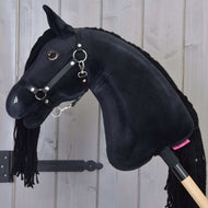 Hobby Horse Maximus met zwart halster van Hobby Horse LarDen heeft glanzende knoopogen en een manen van garen, gemonteerd op een houten stok, getoond voor een wand van lichte houten planken.