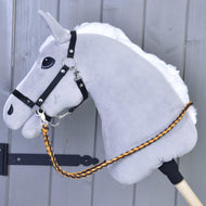 Teugels Gebreid Pomello van Hobby Horse LarDen op een grijs Hobby Horse met witte manen, zwart hoofdstel en gevlochten oranje en bruine teugels van polypropyleen, gemonteerd op een houten stok tegen een grijze houten achtergrond.