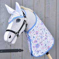 Set Vanessa NEW van Hobby Horse LarDen met een grijze hobby horse met een zwart hoofdstel, een bloemige dekenset met blauwe bies en een bijpassend oornetje, allemaal getoond tegen een houten achtergrond.