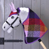Set Herfst Ruit 2 van Hobby Horse LarDen op een pluchen Hobby Horse met grijze snoet, zwart hoofdstel en een kleurrijke patchwork geruite halsbedekking, gemonteerd op een houten stok, getoond tegen een houten wand.