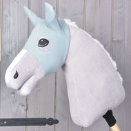 Hobby Horse LarDen "Hobby Horse Masker Stekelig" toont een grijze pluche Hobby Horse met een lichtblauw hoofdstel, witte manen en beschermend masker op een houten stok, weergegeven tegen een lichte houten plankachtergrond.