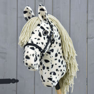 Hobby Horse Lord Valentine met zwart halster van Hobby Horse LarDen met een zwart-wit gevlekte vacht, manen van garen en een zwart halster, tegen een grijze houten achtergrond.