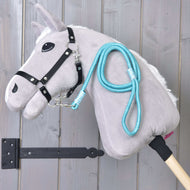 Hobby Horse - touw streep Atlantis van Hobby Horse LarDen met een grijze pluchen kop met zwart hoofdstel en blauwe touwriem, gemonteerd op een houten stok en getoond tegen verticale houten planken.