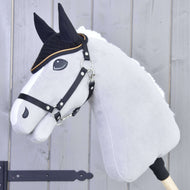 Grijze Hobby Horse van Hobby Horse LarDen met zwarte teugels en witte manen draagt Oornetje gehaakt Black Gold voor insectenbescherming, met zwarte gezichtsdetails, tegen een lichte houten achtergrond.