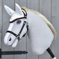 Oornetje Speedy van Hobby Horse LarDen, een realistische grijze Hobby Horse met zwart hoofdstel, witte manen en wit oornetje voor vliegenbescherming, gemonteerd op een houten stok voor een lichtgrijze houten wand.