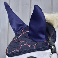Close-up van een paard dat Oornetje Roze Hart van Hobby Horse LarDen draagt voor stijlvolle vliegenbescherming, met roze hartontwerpen en een zwarte band, tegen een lichte houten achtergrond.