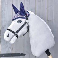Oor Bonnet Flower van Hobby Horse LarDen op een pluchen Hobby Horse met een lichtgrijs hoofd, zwart hoofdstel en glinsterende paars-zilveren oorbescherming tegen insecten, getoond tegen een houten achtergrond.