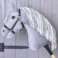 Het grijze Hobby Horse Calypso met Zwart Halster van Hobby Horse LarDen, geïnspireerd op het Nederlands warmbloed, heeft witte manen van garen en is gemonteerd op een houten stok, leunend tegen een lichtgekleurde houten wand.