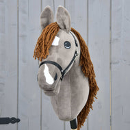 Hobby Horse Chanell met zwart halster van Hobby Horse LarDen, met grijze vacht, bruine garenmanen, witte vlekken op het gezicht, grote expressieve ogen, getoond tegen een grijze houten achtergrond.