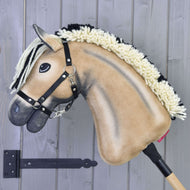 Een lichtbruine en zwarte Hobby Horse LarDen Colby met een zwart halster en manen van garen is gemonteerd op een houten stok tegen een grijze houten wand.