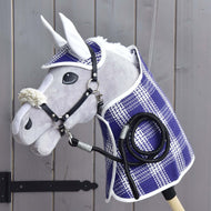Set Cube (Deken, Oornetje, longeerlijn, halster met bont) van Hobby Horse LarDen, met een deken, oornetje, leadrope en halster met bont, is getoond op een houten wand naast een zwart scharnier van een poort. De accessoires benadrukken de kwaliteit en charme van de producten van Hobby Horse LarDen.