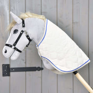 Deken Crème Parel van Hobby Horse LarDen op een pluchen Hobby Horse met een grijze kop, zwart hoofdstel en een crème parel deken met blauwe rand op een houten stok, getoond tegen een grijze houten wand.