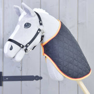 Hobby Horse LarDen Deken Flag, een grijze hobby horse-speelgoed met een zwart hoofdstel en gewatteerde deken met oranje bies, gemonteerd op een houten stok voor een grijze houten schutting.