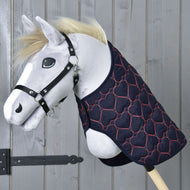 Een pluchen Hobby Horse met een zwart halster en de gewatteerde Hobby Horse-deken Deken Pink Heart van Hobby Horse LarDen, versierd met roze hartjes, geposeerd tegen een houten achtergrond.