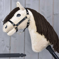 Hobby Horse Frederik LD met zwart halster van Hobby Horse LarDen met een pluchen Mustang-hoofd, bruine manen van garen, zwart halster en teugels op een stok, getoond tegen een achtergrond van houten planken.