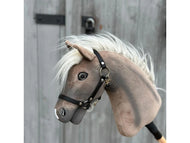 Hobby Horse Happy Boy met zwart halster van Hobby Horse LarDen, een grijs-witte Hannoveraner Pferd Hobby Horse met zwart halster en witte manen, afgebeeld tegen een houten achtergrond met metalen scharnieren en een grendel.