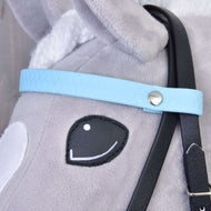 Close-up van het gezicht van een grijs pluchen speelgoedpaard met een gestikt zwart oog, wit oor en het Compleet hoofdstel zonder neusriem Licht Blauw van Hobby Horse LarDen, met een lichtblauwe riem met zilveren knop en afneembare zwarte teugels.