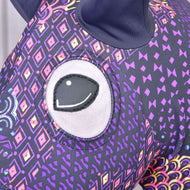 Close-up van het Hobby Horse LarDen beschermpak Mandala (Lycra) met een groot geborduurd oog en paarse stof met kleurrijke geometrische en ruitpatronen; bovenaan is een donker oor zichtbaar.