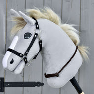 The Cordeo Chocolate by Hobby Horse LarDen is a gray plush hobby horse with a black bridle and cream rope mane on a wooden stick, shown against a gray wooden panel background.