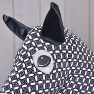 Een close-up van het Hobby Horse beschermpak DeLuxe (Lycra) van Hobby Horse LarDen toont de wasbare zwart-witte geometrische lycrastof, grote zwarte oren en een gestikt oog tegen een lichte houten achtergrond.