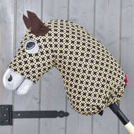 Hobby Horse Beschermpak Luxus Design van Hobby Horse LarDen met een zwart-beige patroonkop, vilten oren, opgezet oog, witte snuit en wasbare materialen, alles gemonteerd op een houten stok tegen een grijze wand.