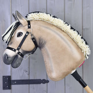 Hobby Horse Ozzy met zwart halster van Hobby Horse LarDen heeft een beige pluchen gezicht, manen van crème- en zwart garen en is gemonteerd op een houten stok, getoond tegen een grijze houten achtergrond.
