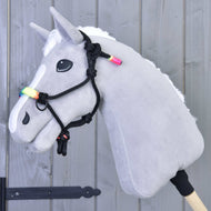 The Hobby Horse LarDen Rope halter Rainbow is a gray hobby horse with a white mane, rainbow-colored beads, and a black rope halter on a wooden stick, shown against a light gray wooden wall.