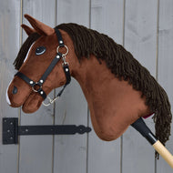 Hobby Horse Rocky met Zwart Halster van Hobby Horse LarDen, een bruine pluchen stokpaard, weergegeven naast een grijs houten wand.