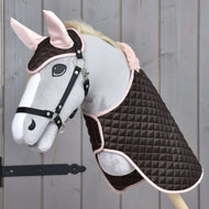 Set Thermo Sweety van Hobby Horse LarDen met een pluche hobby horse met hoofdstel, gekleed in een gewatteerde bruin-roze deken en bijpassende oornetje-set, getoond tegen een houten achtergrond.