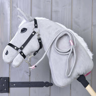 The Hobby Horse LarDen "Hobby Horse - rope stripe Tizian" in gray with a black bridle, white mane, and light wooden stick rests against a gray wall. A coiled leash—perfect for play—hangs from its neck.