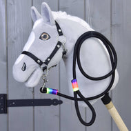 The Hobby Horse LarDen "Hobby Horse - Lead rope Rainbow" is a gray hobby horse with a white mane, black bridle, reins, and a rainbow-taped lead rope around its neck, displayed against wooden paneling.