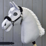 Zwart halster met zwart bont - kunstleer van Hobby Horse LarDen op een pluche lichtgrijs paard met een zwart kunstleren halster en grote geborduurde ogen, getoond tegen een grijze houten achtergrond.