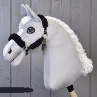 Zwart halster met compleet zwart bont - kunstleer van Hobby Horse LarDen op een houten stok, gefotografeerd tegen een achtergrond van houten panelen.